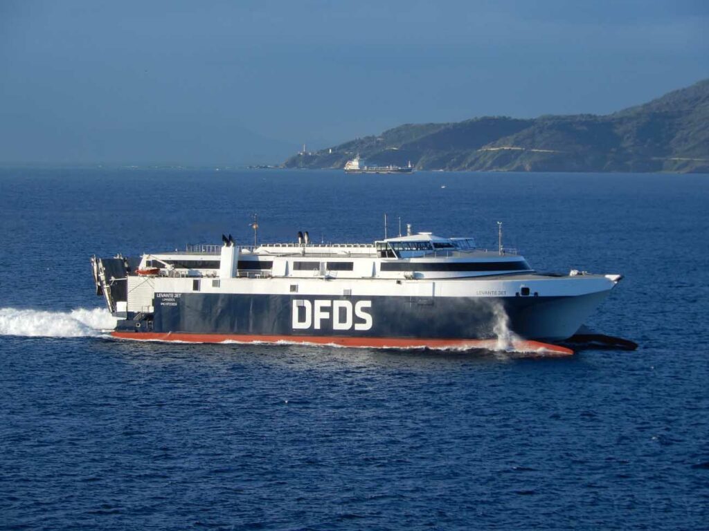 Le catamaran HSC Levante Jet de DFDS est photographié alors qu'il navigue en pleine mer. En arrière-plan, se trouve le phare de Corbière, l'un des phares qui entoure l'île de Jersey.